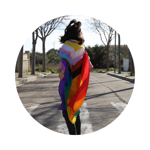 Imagen de una persona con una bandera lgtbyq+ sobre los hombros, en medio de una carretera